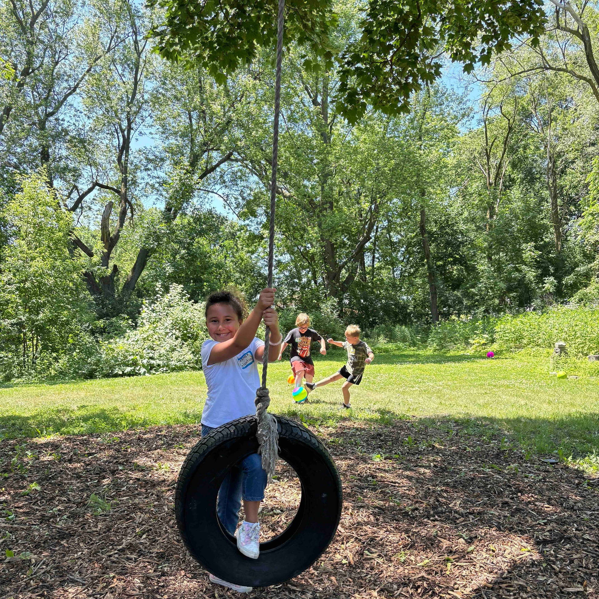 Child on a tire swing in a park with trees and grass in the background