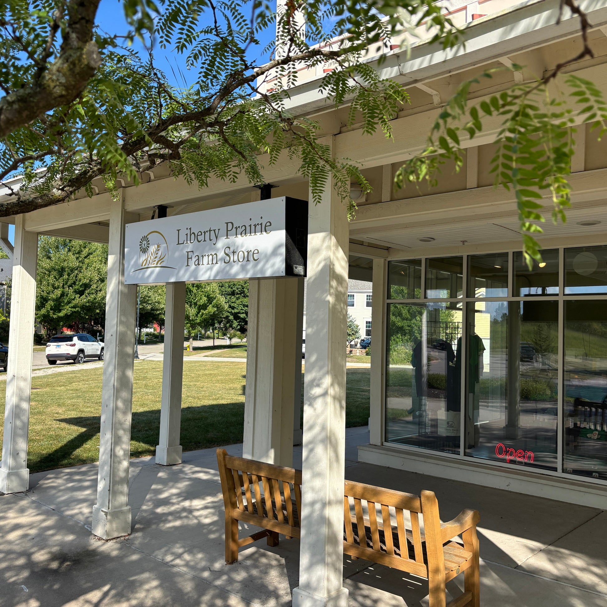 Liberty Prairie Farm Store entrance with a sign and wooden benches on a sunny day.