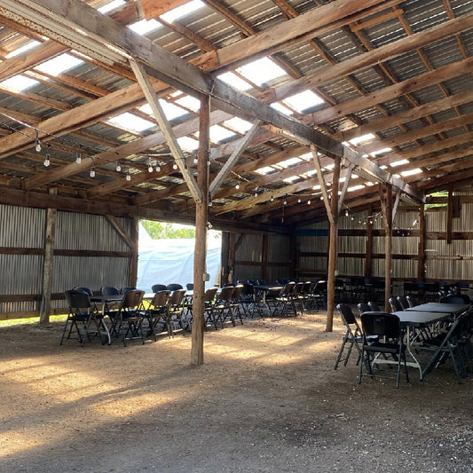 Interior view of The Tall Barn featuring rustic wooden beams, tables, and chairs under a skylit roof.